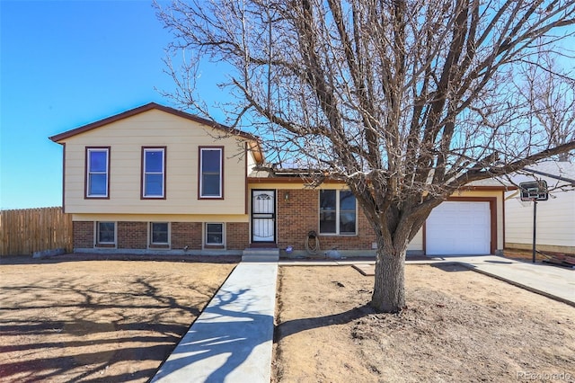 tri-level home featuring concrete driveway, brick siding, an attached garage, and fence