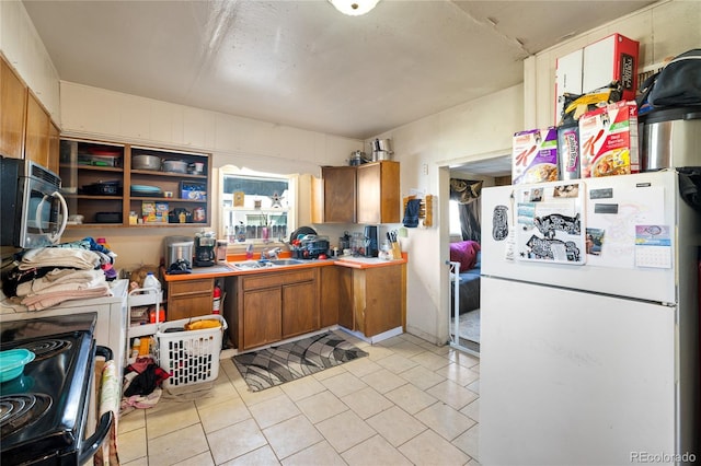 1437 Cypress St, Pueblo, CO 81004 - kitchen featuring freestanding refrigerator, stainless steel microwave, black range with electric cooktop, light tile patterned flooring, and brown cabinetry