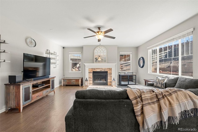 living area featuring a stone fireplace, baseboards, a ceiling fan, and wood finished floors