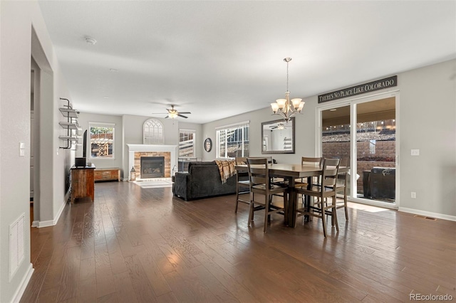 dining area featuring ceiling fan with notable chandelier, visible vents, a fireplace, and dark wood-style flooring