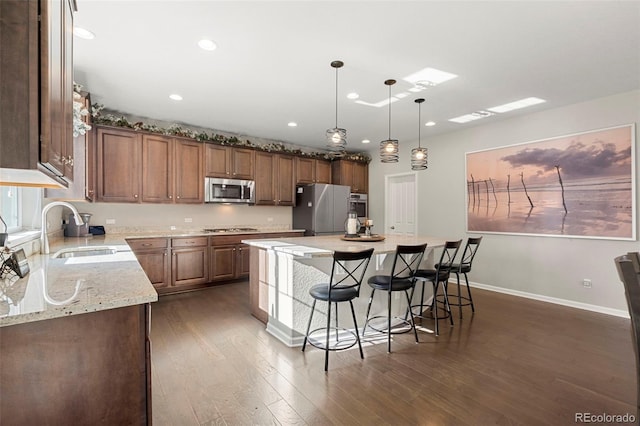 kitchen with light stone countertops, dark wood-style floors, a breakfast bar, a sink, and appliances with stainless steel finishes