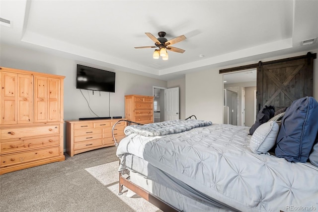 bedroom featuring visible vents, ceiling fan, light colored carpet, a barn door, and a tray ceiling