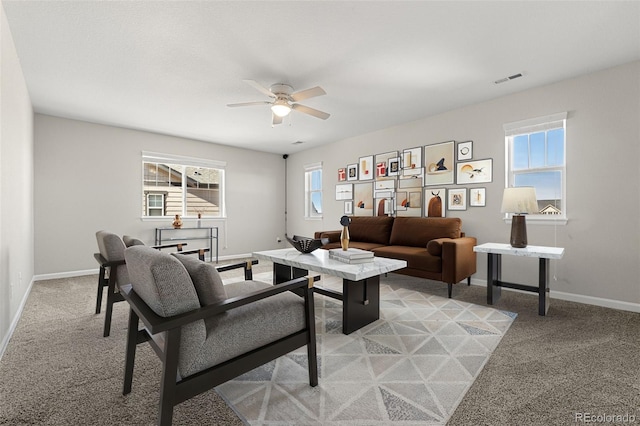 living area featuring plenty of natural light, a ceiling fan, baseboards, and light carpet