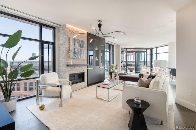 living area with expansive windows, baseboards, wood finished floors, and a stone fireplace