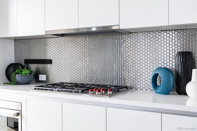 interior details with white cabinets, decorative backsplash, stainless steel appliances, light countertops, and under cabinet range hood