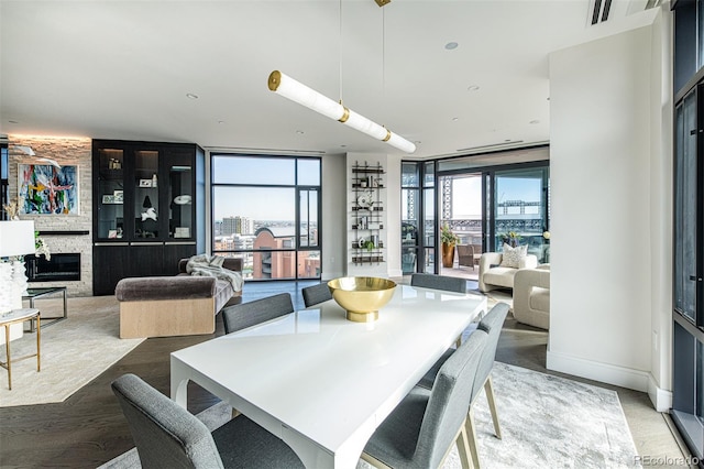 dining space featuring floor to ceiling windows, a stone fireplace, light wood-style flooring, and a healthy amount of sunlight