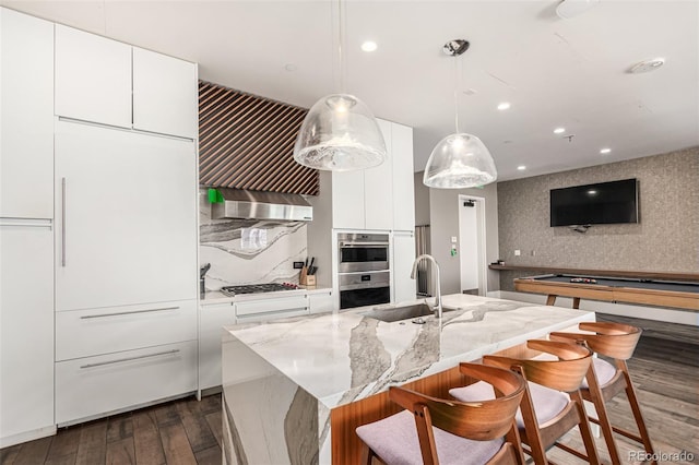 kitchen with dark wood finished floors, wall chimney exhaust hood, modern cabinets, appliances with stainless steel finishes, and a sink