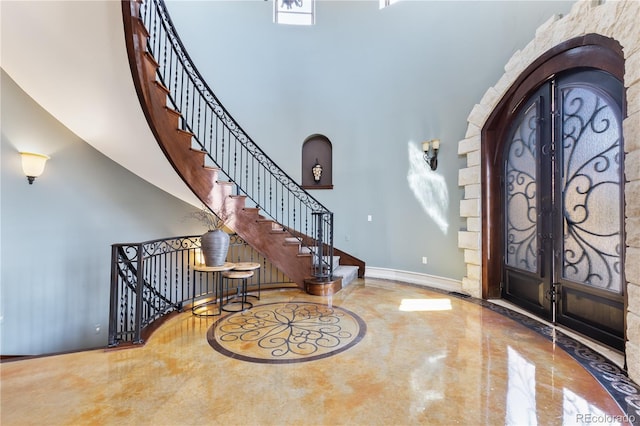 entrance foyer featuring baseboards, arched walkways, marble finish floor, and a towering ceiling