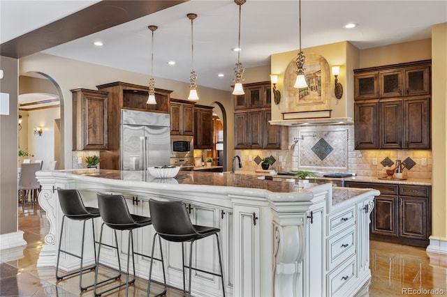 kitchen featuring arched walkways, decorative backsplash, built in appliances, and a kitchen bar