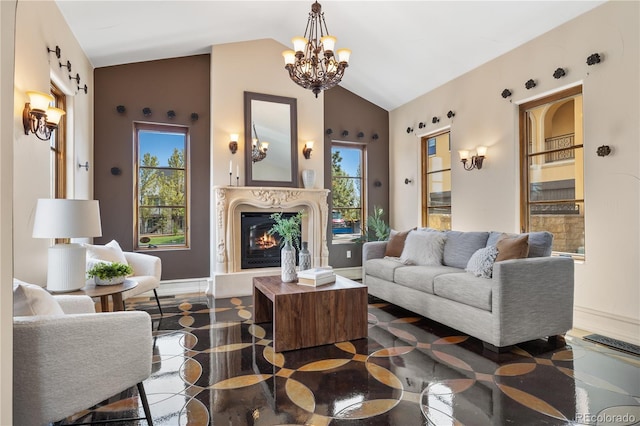 living area with baseboards, a glass covered fireplace, lofted ceiling, and a notable chandelier
