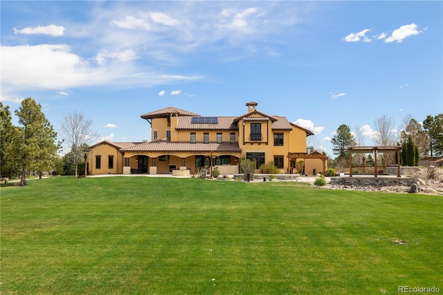 rear view of house with a patio, a lawn, a pergola, and solar panels