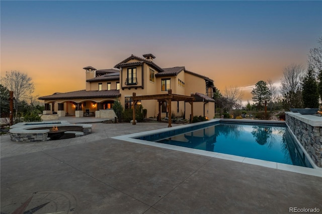 pool at dusk featuring a patio, an in ground hot tub, and an outdoor pool