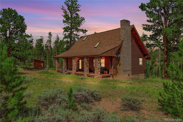 back of property at dusk with a shingled roof, a chimney, and log exterior