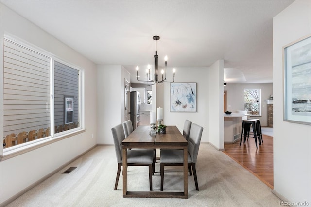 dining area featuring light carpet, a chandelier, visible vents, and baseboards