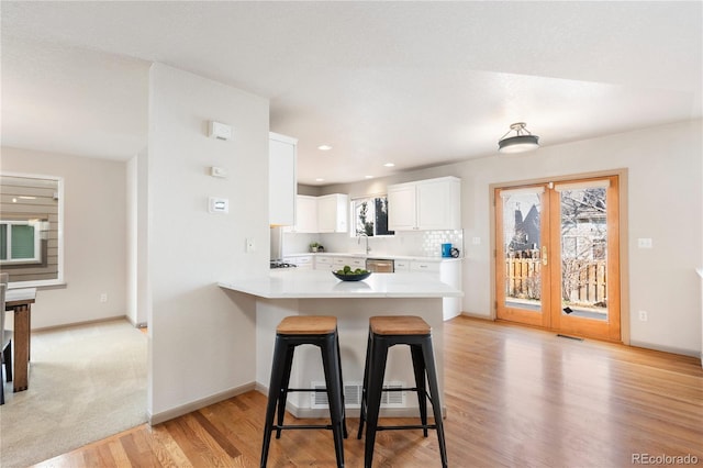 kitchen featuring a peninsula, a kitchen breakfast bar, white cabinets, light countertops, and a wealth of natural light