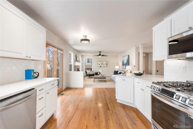 kitchen with light wood-style flooring, appliances with stainless steel finishes, a ceiling fan, open floor plan, and white cabinets