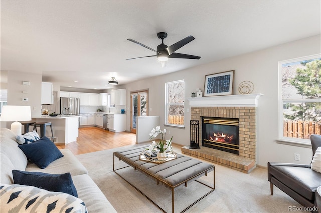 living room with a brick fireplace, a ceiling fan, and baseboards