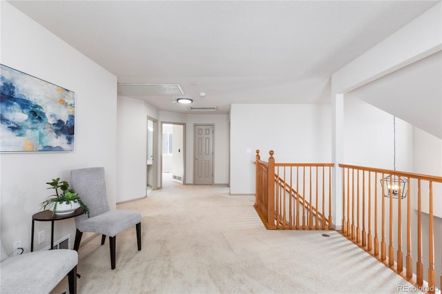 living area with an upstairs landing, attic access, a chandelier, and light colored carpet