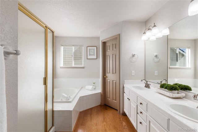 full bathroom with double vanity, a garden tub, a sink, and wood finished floors