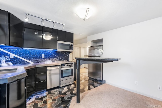 kitchen featuring dark colored carpet, decorative backsplash, appliances with stainless steel finishes, modern cabinets, and dark cabinetry