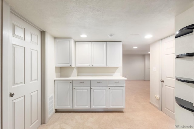 kitchen featuring a textured ceiling, light countertops, light colored carpet, and white cabinets