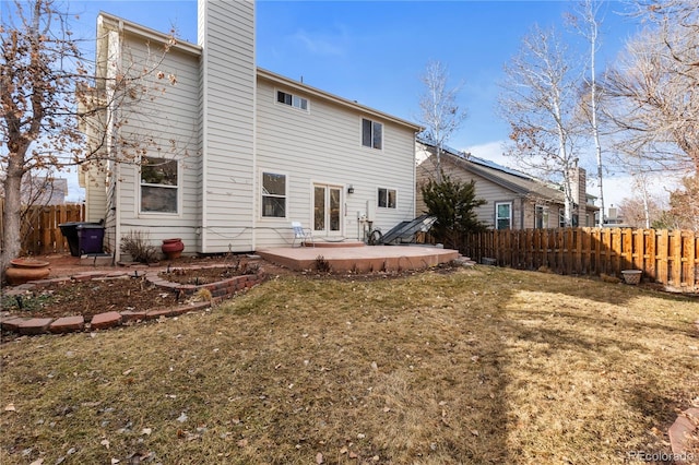 back of house featuring a fenced backyard, a chimney, a lawn, and a patio