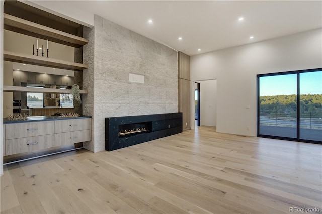 unfurnished living room with built in features, a tiled fireplace, a high ceiling, light wood-style floors, and recessed lighting