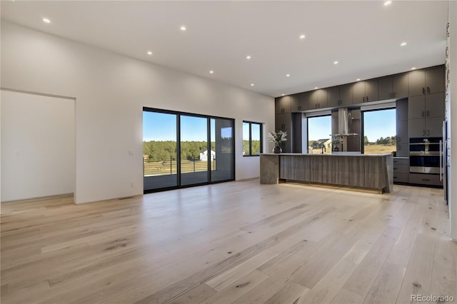 unfurnished living room with a high ceiling, light wood-type flooring, and recessed lighting