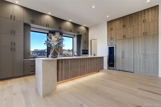 kitchen featuring an island with sink, light wood-style floors, beverage cooler, and light countertops