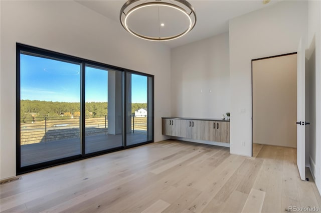 unfurnished room with light wood-style floors, a high ceiling, and visible vents