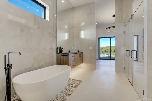 bathroom with tile walls, a freestanding bath, a shower stall, vanity, and tile patterned flooring