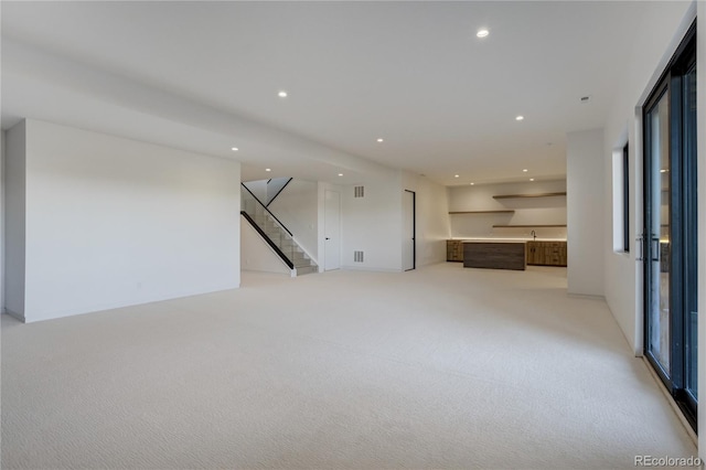 unfurnished living room with visible vents, stairway, light colored carpet, and recessed lighting