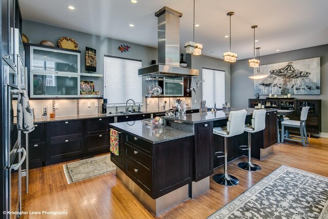 460 N Garfield St, Denver, CO 80206 - kitchen with island range hood, dark cabinetry, a center island, a breakfast bar area, and dark stone countertops