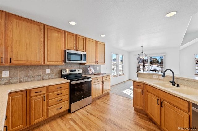 kitchen featuring tasteful backsplash, sink, hanging light fixtures, stainless steel appliances, and light hardwood / wood-style flooring