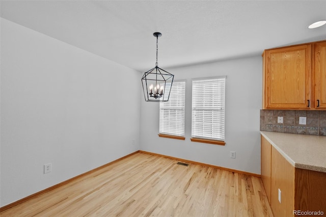 unfurnished dining area featuring an inviting chandelier and light hardwood / wood-style floors