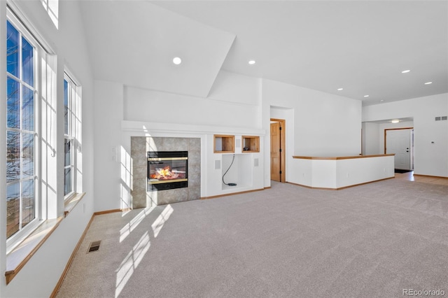 unfurnished living room with a tiled fireplace, a towering ceiling, and light carpet