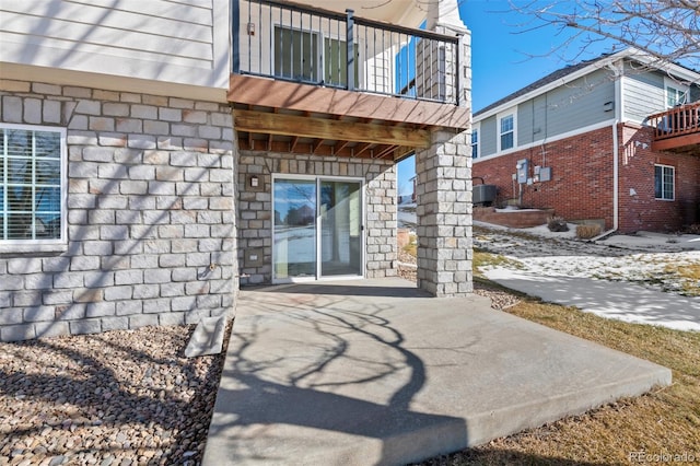 view of exterior entry featuring a balcony, central AC unit, and a patio area