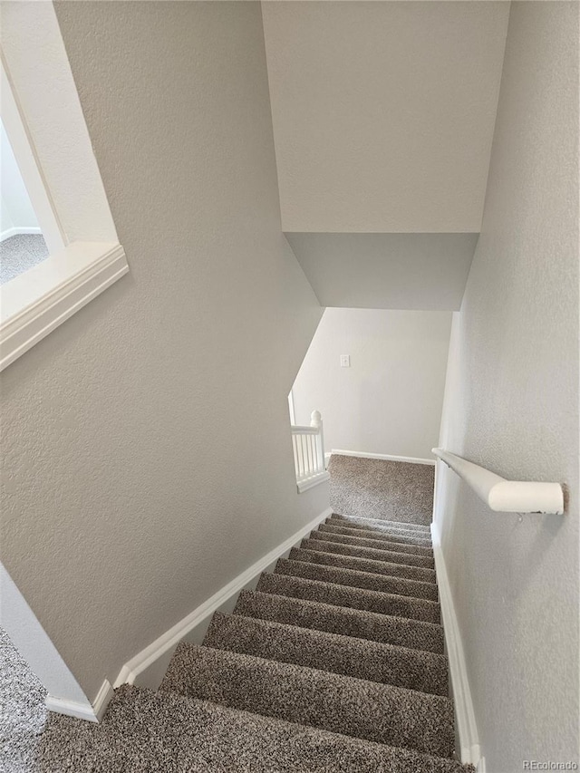 staircase with baseboards, a textured wall, and carpet floors