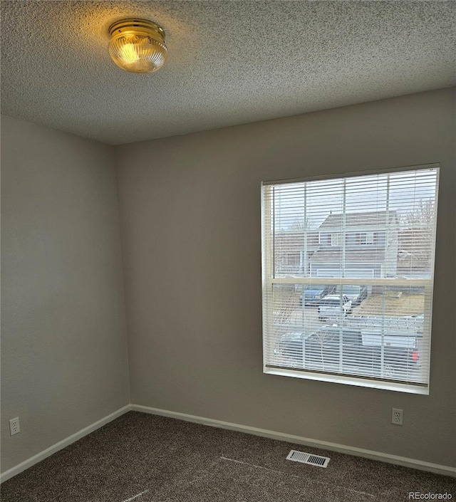 spare room featuring visible vents, carpet floors, a textured ceiling, and baseboards