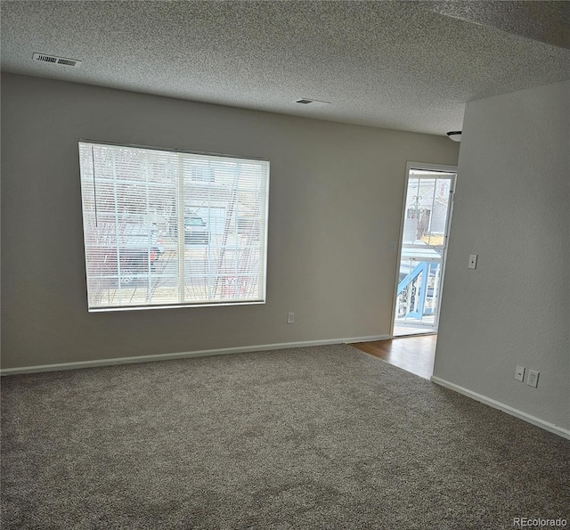 carpeted empty room featuring visible vents, a textured ceiling, and baseboards