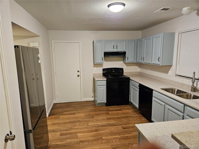 kitchen with visible vents, black appliances, a sink, under cabinet range hood, and wood finished floors