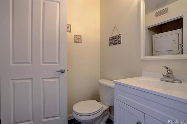 bathroom with vanity, stacked washer and clothes dryer, and toilet