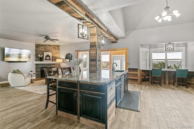 kitchen with light stone countertops, a fireplace, sink, hanging light fixtures, and a center island with sink