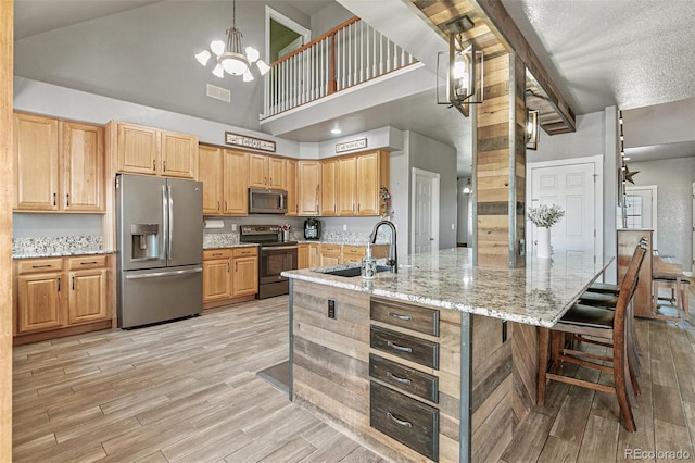 kitchen featuring stainless steel appliances, sink, high vaulted ceiling, a notable chandelier, and light stone counters