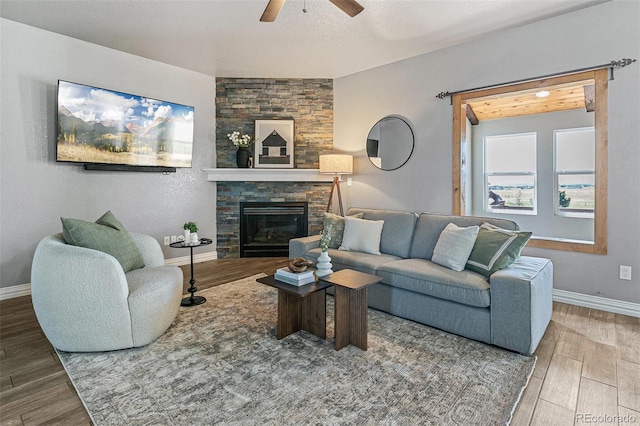 living room featuring ceiling fan, a stone fireplace, and a textured ceiling