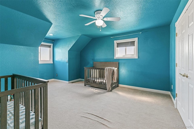 carpeted bedroom with a textured ceiling, vaulted ceiling, ceiling fan, and a nursery area