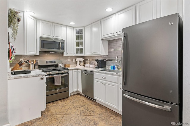 kitchen with appliances with stainless steel finishes, sink, white cabinets, tasteful backsplash, and light tile patterned floors