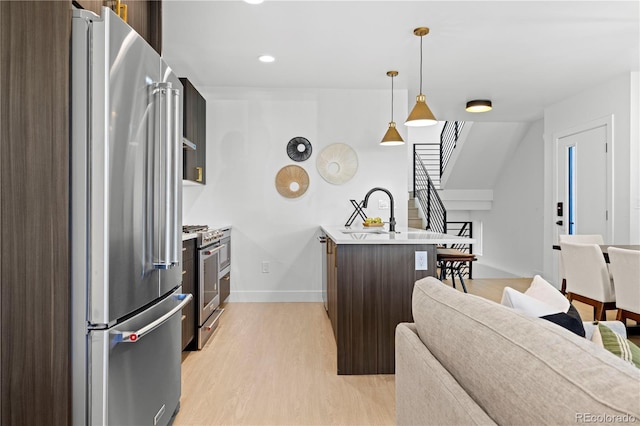 kitchen with sink, dark brown cabinets, stainless steel appliances, decorative light fixtures, and light wood-type flooring