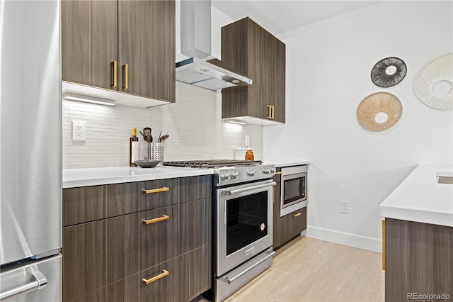 kitchen with backsplash, light hardwood / wood-style floors, dark brown cabinetry, stainless steel appliances, and wall chimney range hood