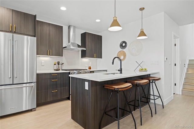 kitchen featuring high quality fridge, wall chimney exhaust hood, sink, and light wood-type flooring